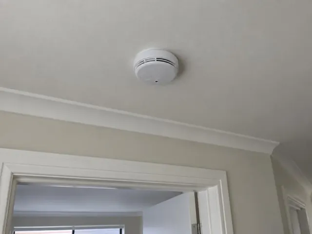 Ceiling-mounted smoke alarm above a doorway in a light-painted hallway in Southport